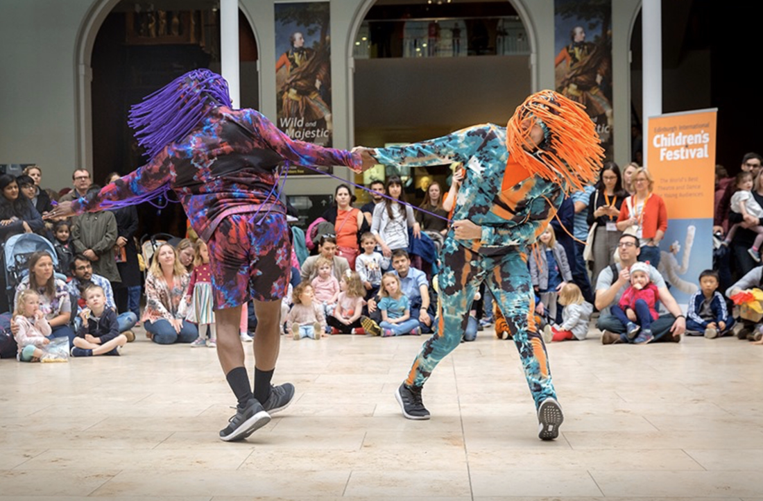 2 dancers in fun costumes designed by Alison Brown  Costume Designer for Edinburgh Children's Festival and Choreographer Vince Virr at National Museums Scotland. Watched by an audience of children and parents.