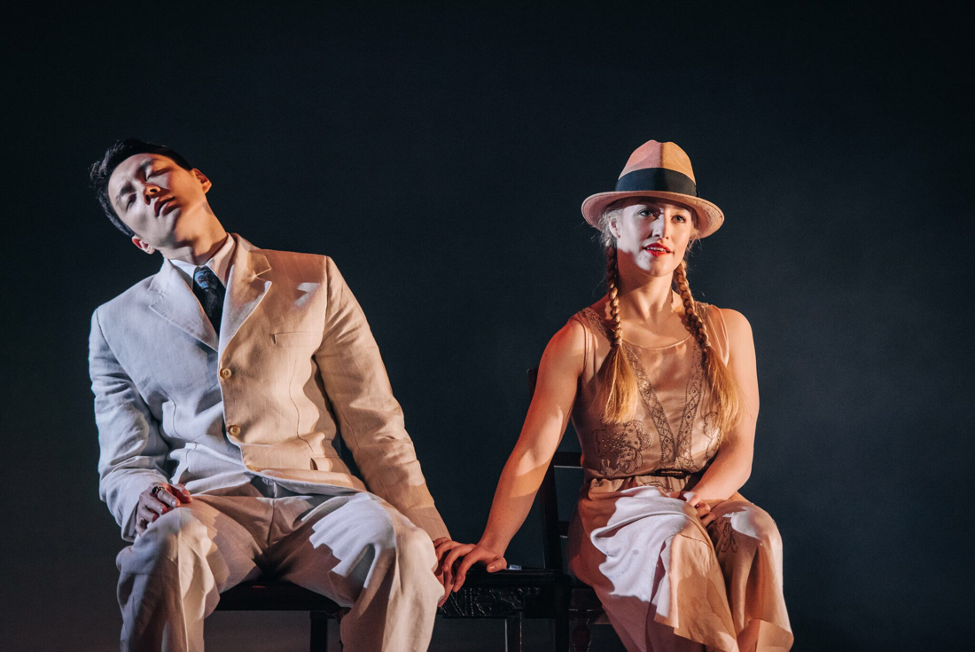 2 dancers are sitting on stage at the Lyceum performing The Lover. The man is wearing a linen suit and the girl is wearing a silk beaded 1920's dress and a straw trilby hat with pigtails. Costumes are designed by Alison Brown Costume Designer.